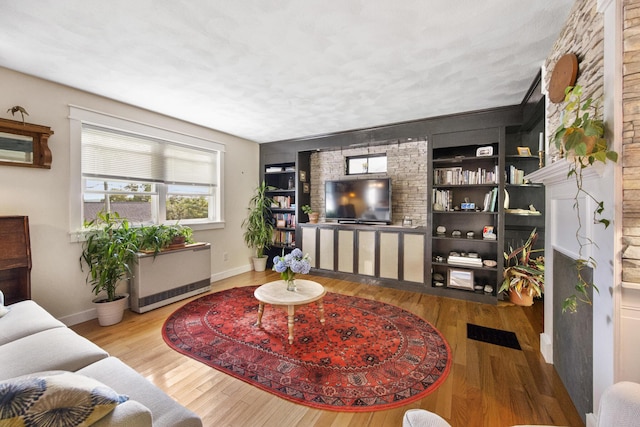 living room featuring radiator heating unit, built in shelves, baseboards, and wood finished floors