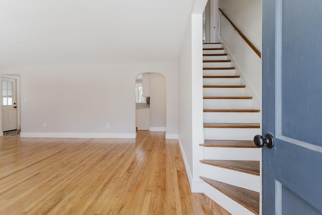 stairway with baseboards, arched walkways, and wood finished floors