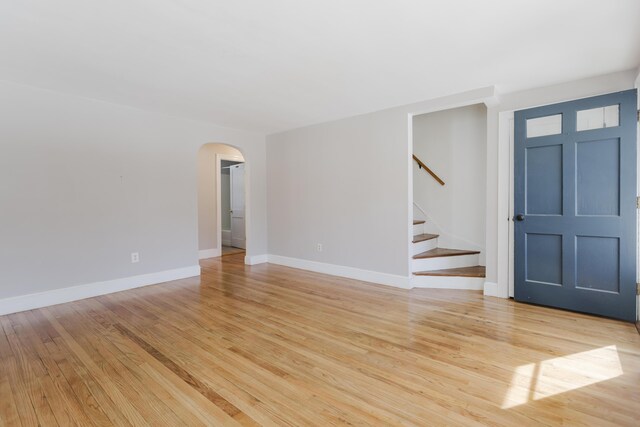 interior space with stairs, baseboards, arched walkways, and light wood-type flooring