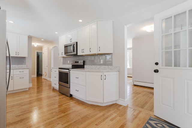 kitchen featuring backsplash, light wood-style flooring, appliances with stainless steel finishes, white cabinets, and a baseboard radiator