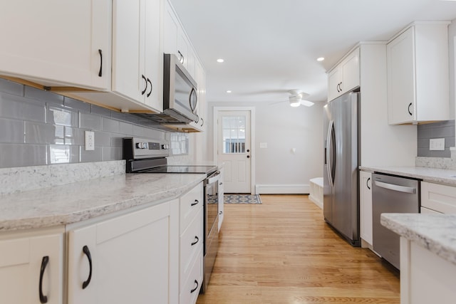 kitchen featuring a ceiling fan, light wood finished floors, stainless steel appliances, white cabinetry, and tasteful backsplash