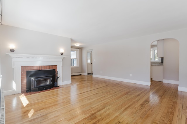 unfurnished living room with arched walkways, baseboard heating, light wood-type flooring, and baseboards