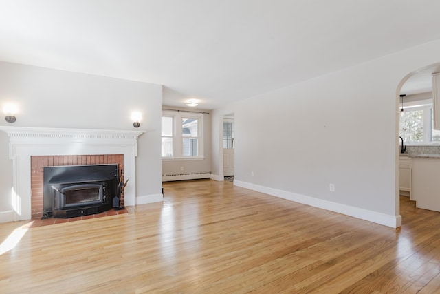 unfurnished living room with light wood finished floors, arched walkways, a baseboard heating unit, and baseboards