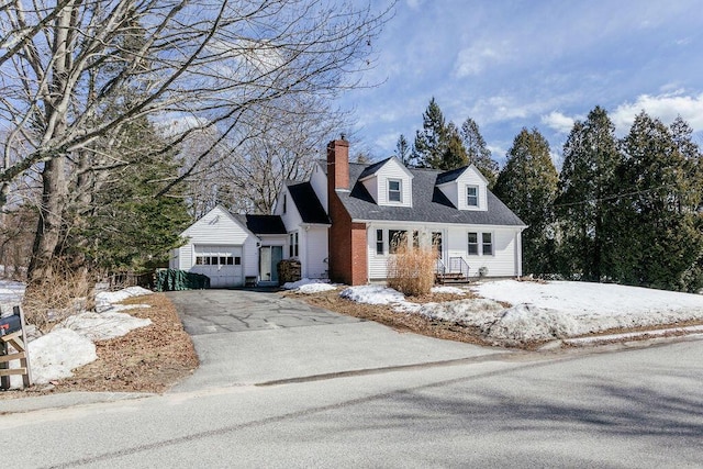 new england style home with aphalt driveway, a chimney, an attached garage, and a shingled roof