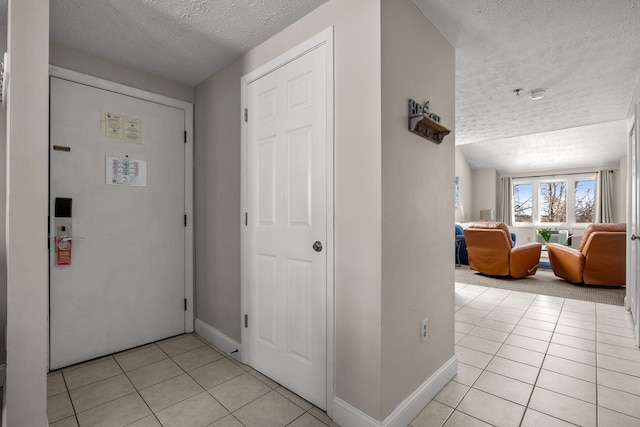 foyer with a textured ceiling, baseboards, and light tile patterned floors