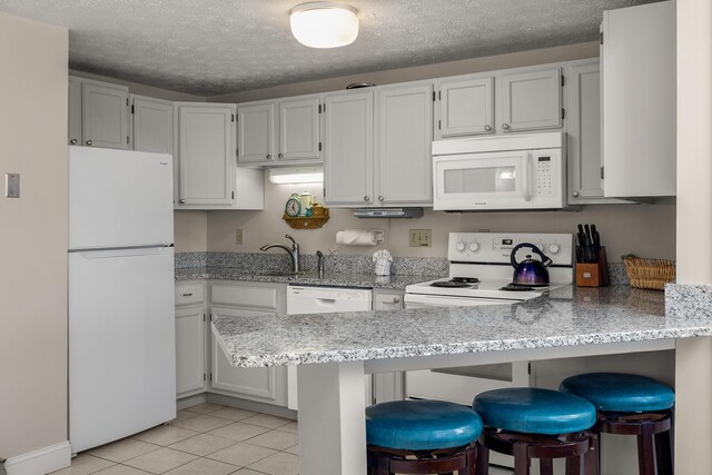 kitchen featuring light tile patterned flooring, a sink, a textured ceiling, white appliances, and a peninsula