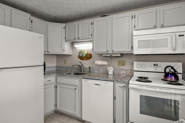 kitchen with light tile patterned floors, a sink, a textured ceiling, light stone countertops, and white appliances