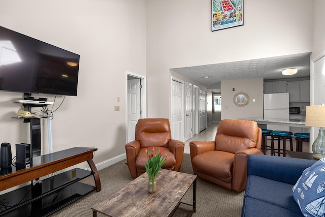 living area featuring light colored carpet, a high ceiling, and baseboards