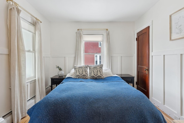 bedroom featuring a decorative wall, multiple windows, light wood-style floors, and a baseboard radiator