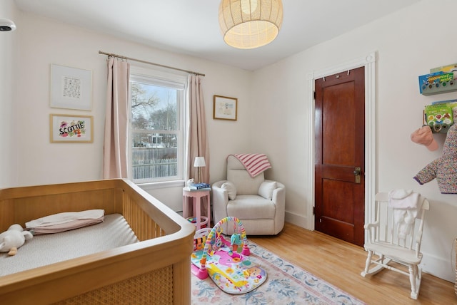 bedroom with baseboards, a nursery area, and wood finished floors