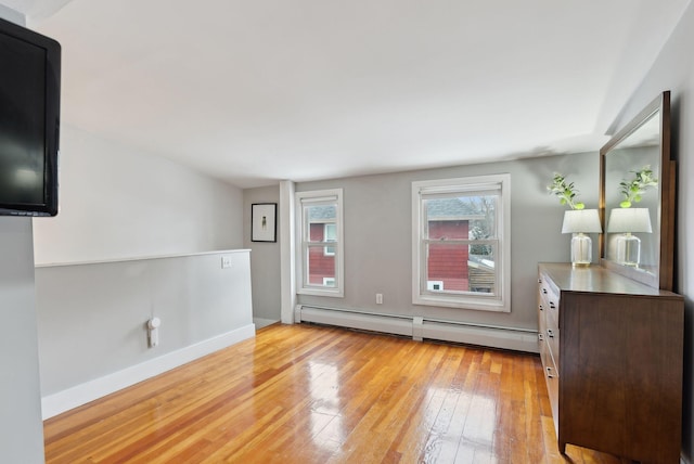 unfurnished room featuring baseboard heating, light wood-style flooring, and baseboards