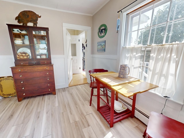 dining room with wainscoting, ornamental molding, baseboard heating, light wood-type flooring, and a decorative wall