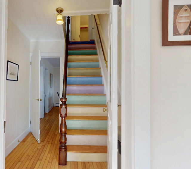 stairs with a baseboard heating unit, ornamental molding, wood finished floors, and baseboards