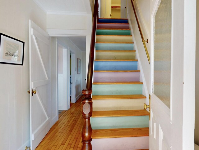 staircase with ornamental molding and wood finished floors