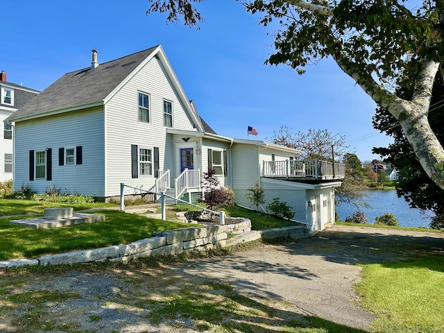 view of front facade featuring aphalt driveway, a front yard, a water view, and an attached garage