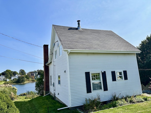 view of home's exterior with a shingled roof, a water view, and a yard