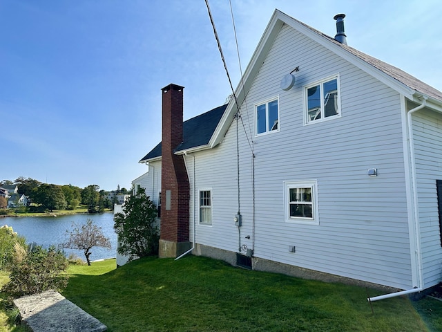 view of side of home featuring a water view, a chimney, and a lawn