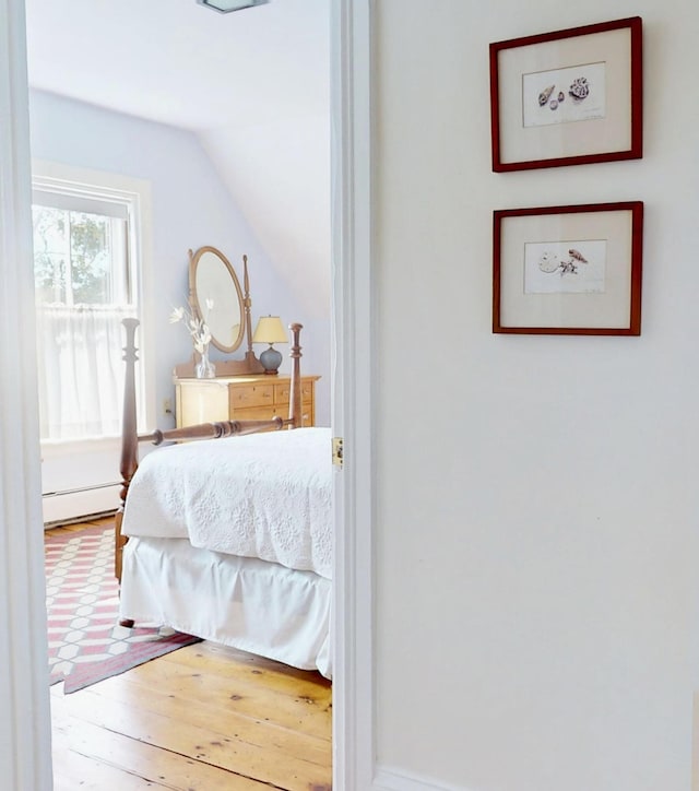 bedroom with lofted ceiling, hardwood / wood-style flooring, and a baseboard heating unit