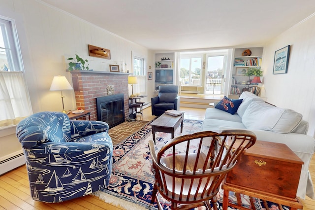 living room with built in shelves, crown molding, a baseboard heating unit, a brick fireplace, and hardwood / wood-style flooring