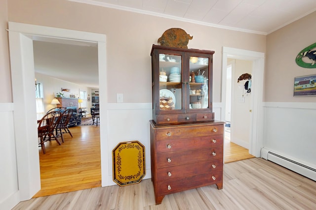 hall featuring a wainscoted wall, crown molding, light wood finished floors, and baseboard heating