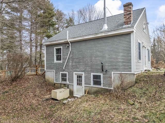 rear view of house featuring roof with shingles and a chimney