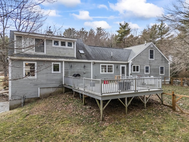 rear view of house featuring a lawn, fence, a shingled roof, a wooden deck, and a chimney