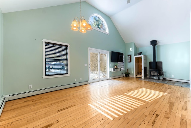 unfurnished living room with a notable chandelier, baseboard heating, a wood stove, and hardwood / wood-style flooring