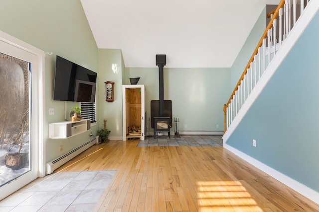 unfurnished living room with baseboards, stairway, light wood-style flooring, a wood stove, and a baseboard radiator