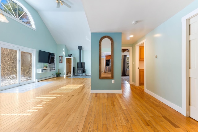 unfurnished living room featuring baseboards, light wood-type flooring, a wood stove, high vaulted ceiling, and a baseboard radiator