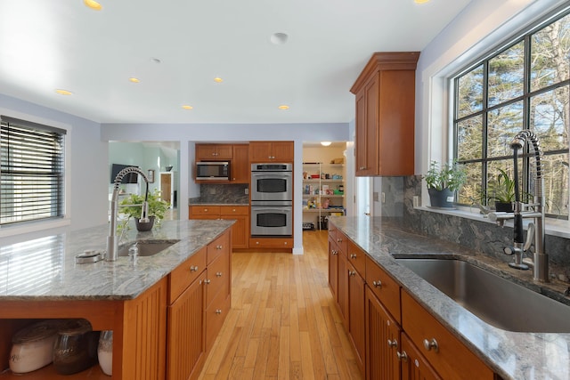 kitchen with a sink, light wood-type flooring, appliances with stainless steel finishes, and brown cabinetry