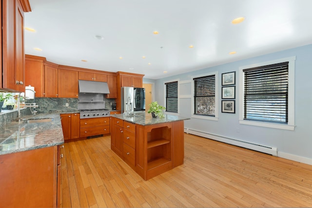 kitchen featuring a baseboard radiator, refrigerator, stainless steel gas stovetop, under cabinet range hood, and brown cabinets