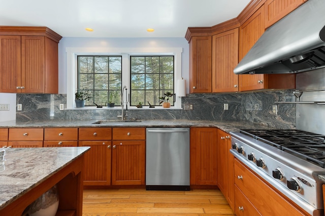 kitchen with dark stone counters, stainless steel appliances, a sink, under cabinet range hood, and brown cabinets