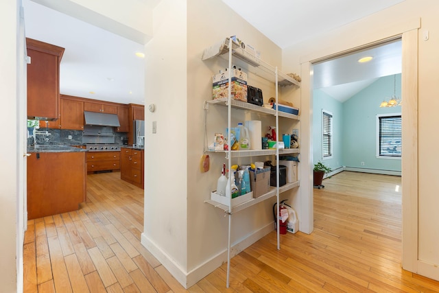 hallway with a baseboard heating unit, baseboards, light wood-type flooring, and lofted ceiling