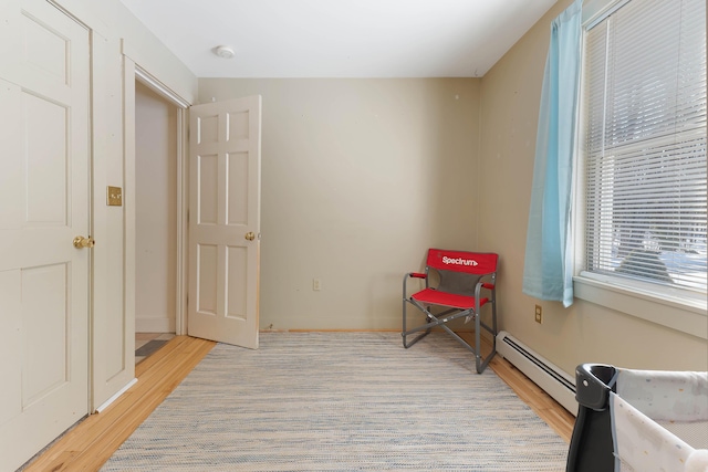 sitting room featuring a baseboard heating unit, baseboards, and light wood-type flooring