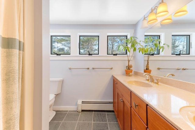 bathroom with baseboards, toilet, double vanity, baseboard heating, and a sink