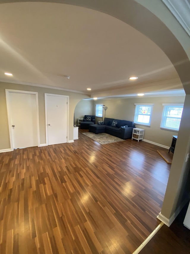 unfurnished living room featuring wood finished floors, arched walkways, and baseboards