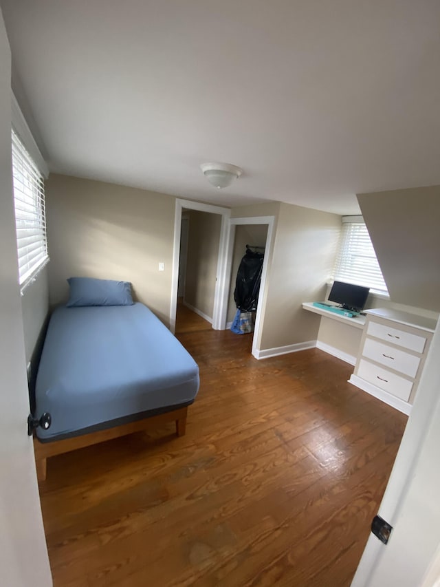 bedroom featuring baseboards, multiple windows, wood finished floors, and built in study area