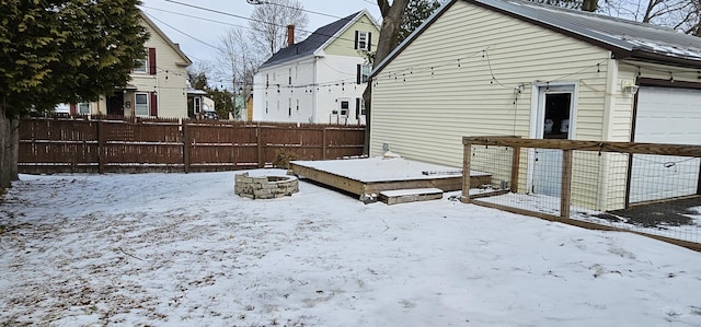 yard layered in snow with a fire pit, fence, and a wooden deck