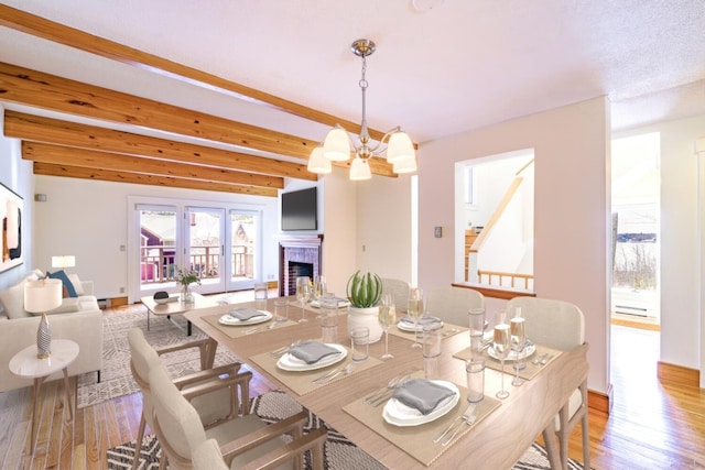 dining area featuring a chandelier, a fireplace, beamed ceiling, and wood finished floors