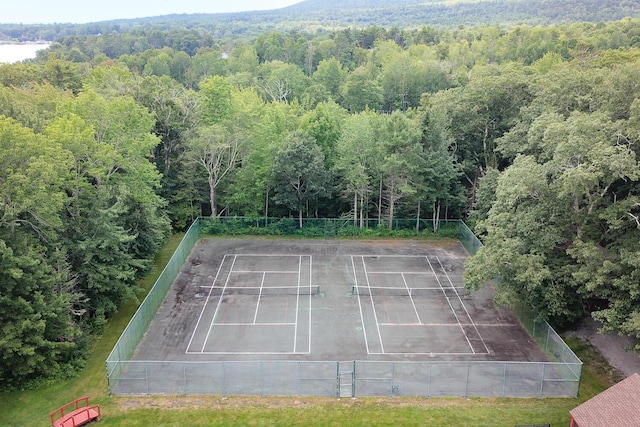 view of tennis court with fence and a view of trees