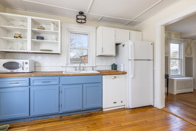 kitchen with light wood-type flooring, blue cabinetry, wood counters, a sink, and white appliances