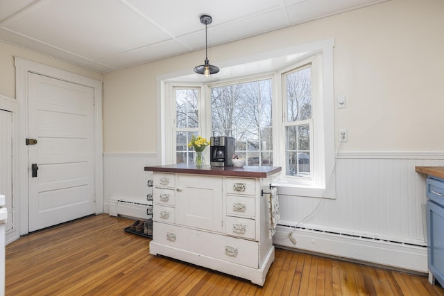 kitchen featuring butcher block countertops, a baseboard radiator, light wood-style floors, and a wainscoted wall