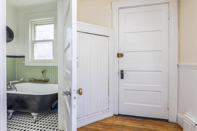 full bath with hardwood / wood-style flooring, a wainscoted wall, and a freestanding bath