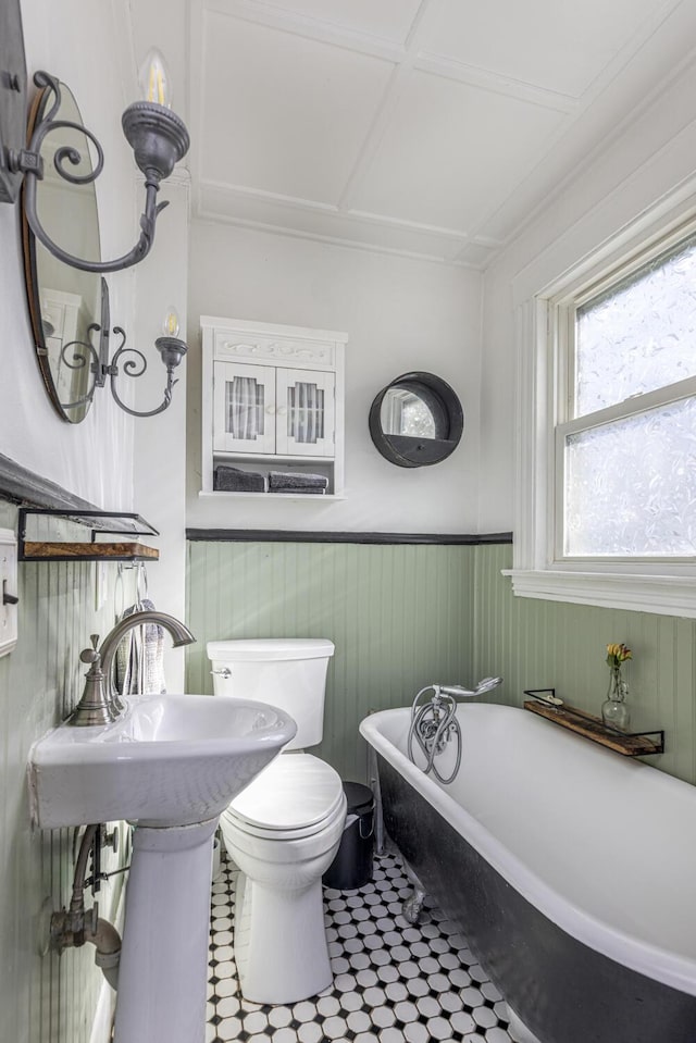 bathroom with a soaking tub, a wainscoted wall, and toilet