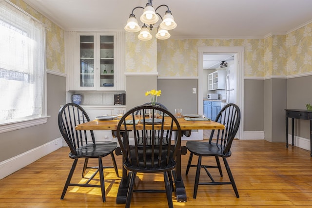 dining area featuring wallpapered walls, wainscoting, light wood finished floors, baseboards, and a chandelier