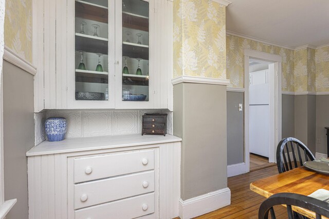 kitchen with wood finished floors, wallpapered walls, light countertops, glass insert cabinets, and white cabinetry