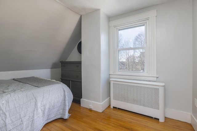 bedroom featuring lofted ceiling, radiator, baseboards, and light wood-type flooring