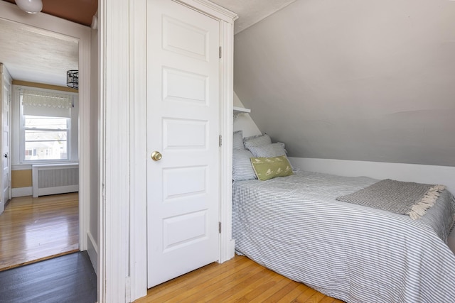 bedroom featuring light wood-type flooring, radiator heating unit, and vaulted ceiling