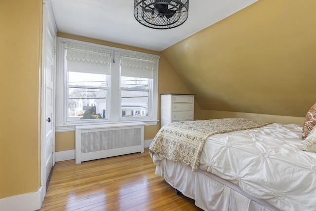 bedroom with radiator, baseboards, lofted ceiling, and wood-type flooring