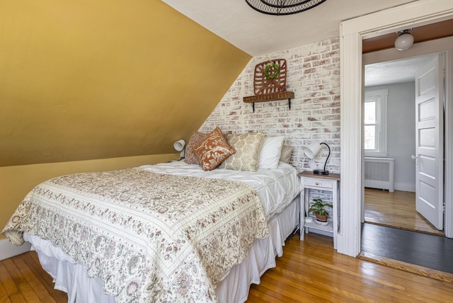 bedroom with radiator heating unit, lofted ceiling, and wood-type flooring